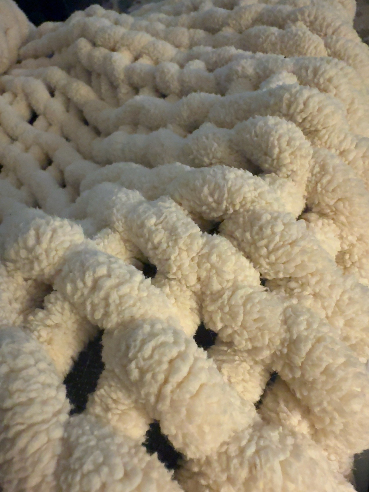 Close-up of a cream-colored blanket with thick, plush yarn and large open knit loops.